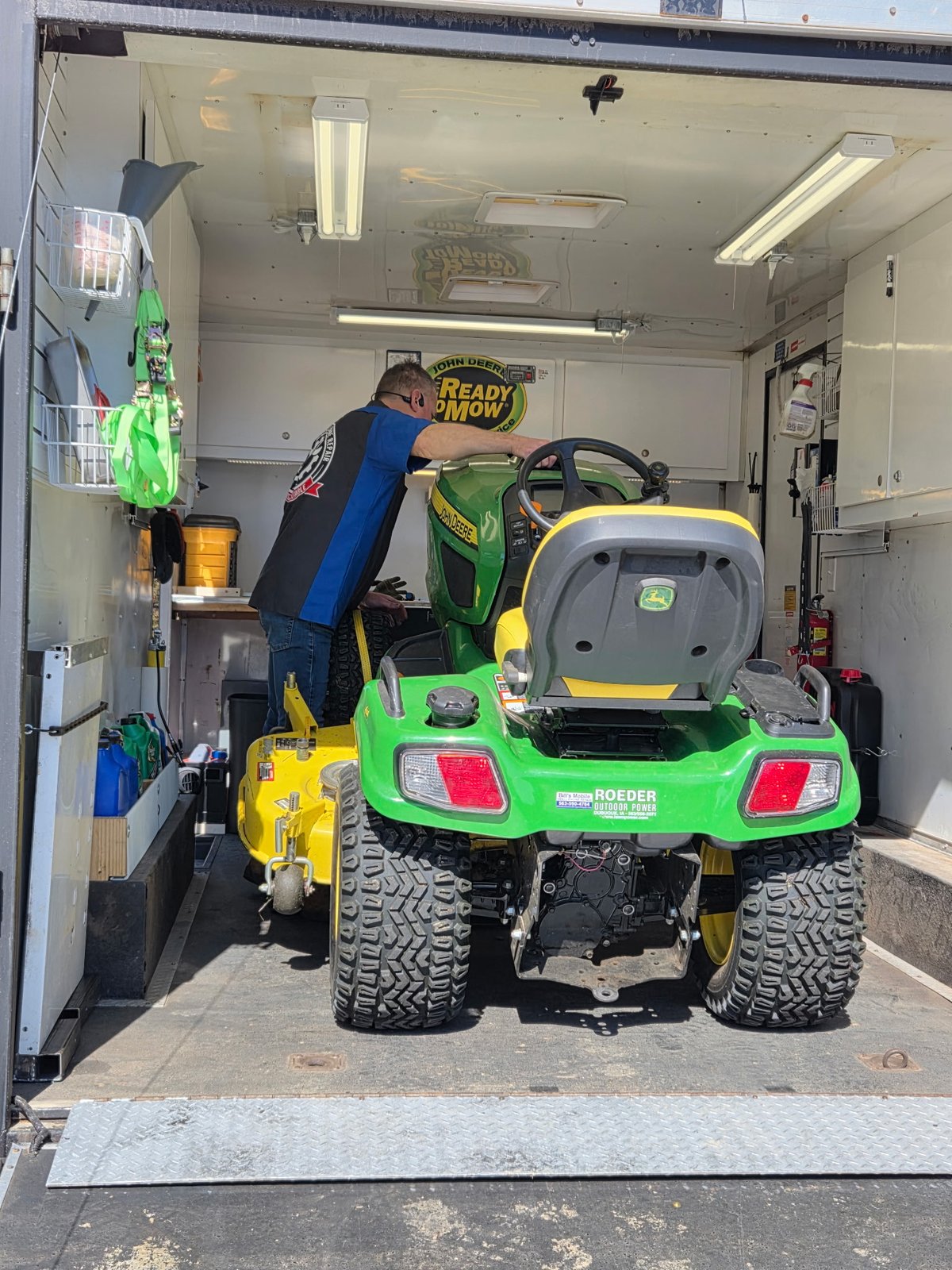 Bill working on a John Deere riding tractor inside the mobile trailer, viewed from the rear of the machine
