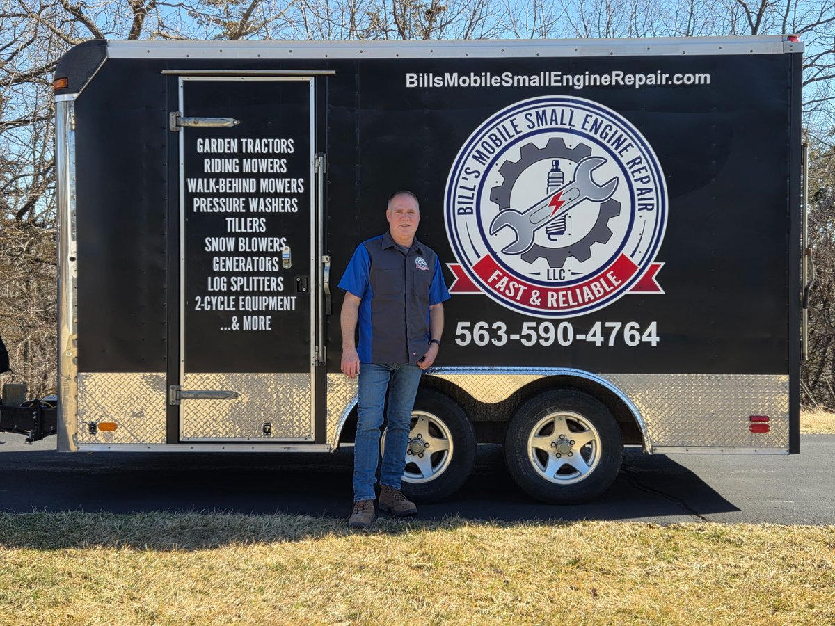 Bill standing in front of the branded mobile repair trailer showing the full services list and company logo
