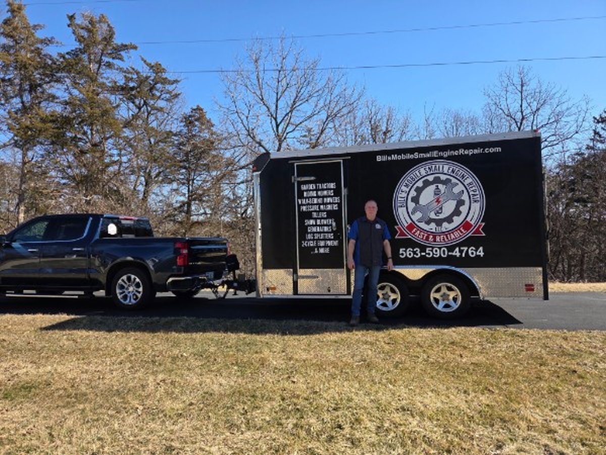 Bill standing beside the branded Bill's Mobile Small Engine Repair trailer hitched to his black Chevrolet truck, ready for on-site service in the Dubuque Iowa area