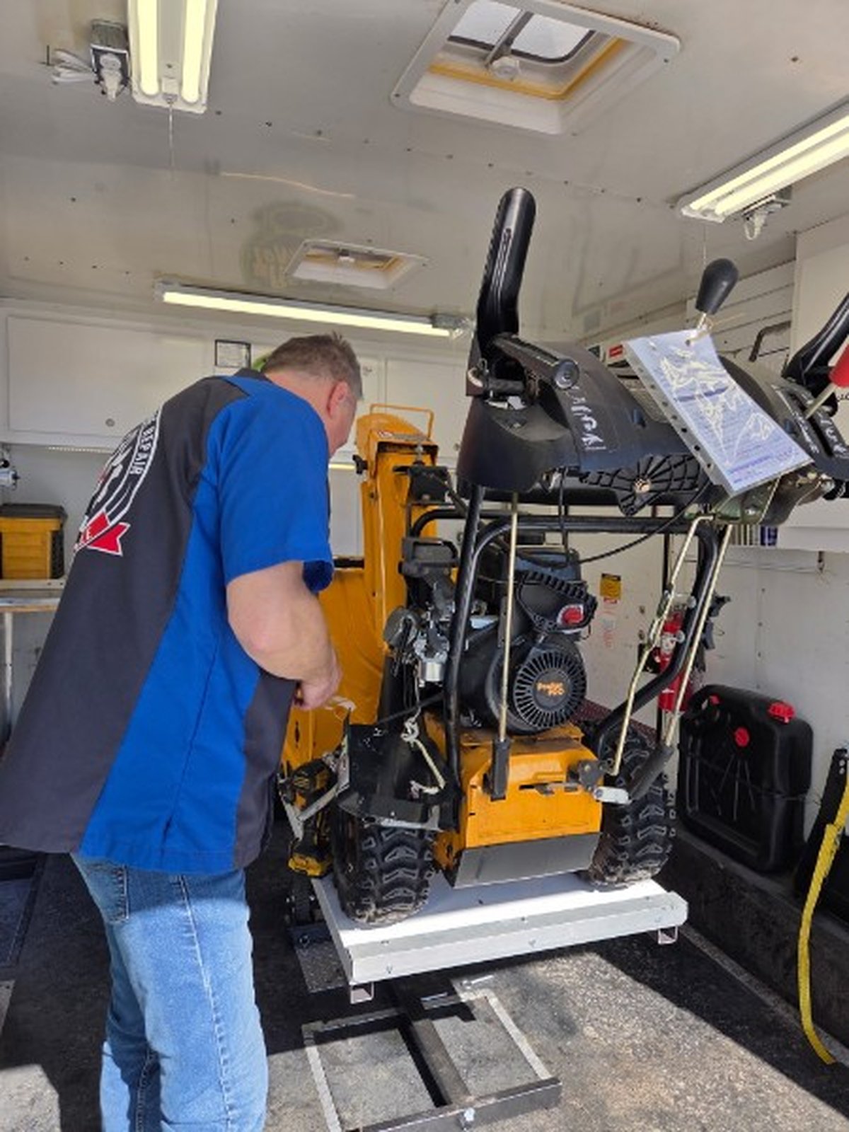 Bill servicing a tracked snowblower on the hydraulic lift inside the mobile repair trailer, close-up view
